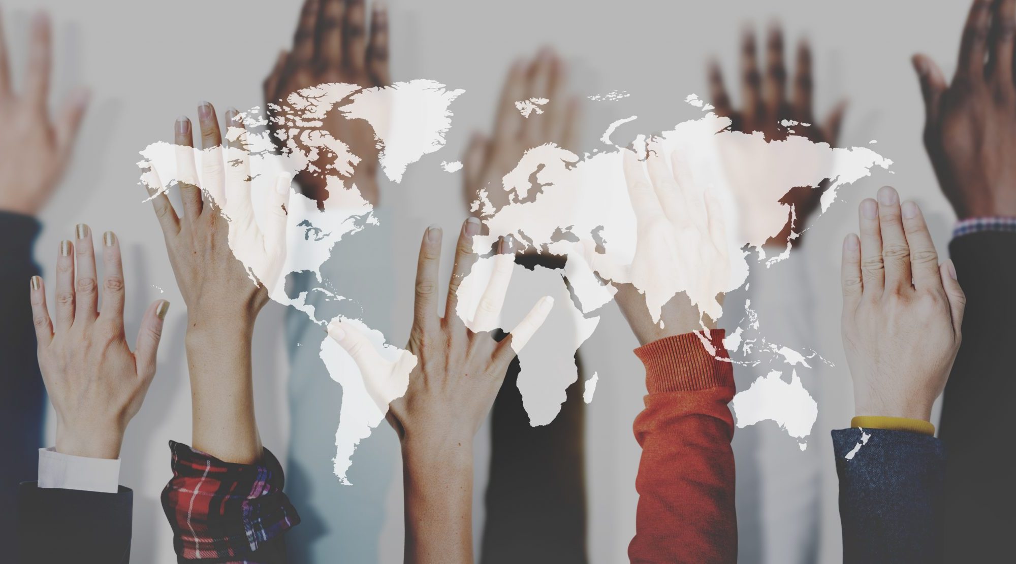 Hands up in the air against a map of the world. Business Impact article for today's education: global commodity and catalyst for cultural diversity