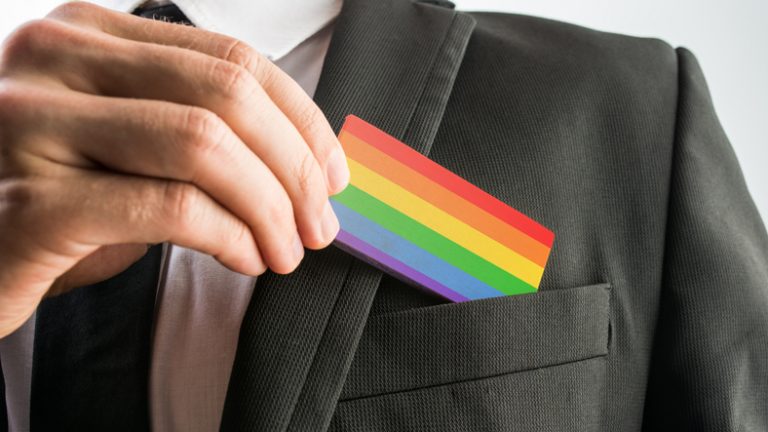 Close up of a business professional putting pride colours, LGBT+ card into the chest pocket of a smart black blazer. BGA webinar for GaYme Changers at work: how the LGBT+ community and their allies are changing the global economy.
