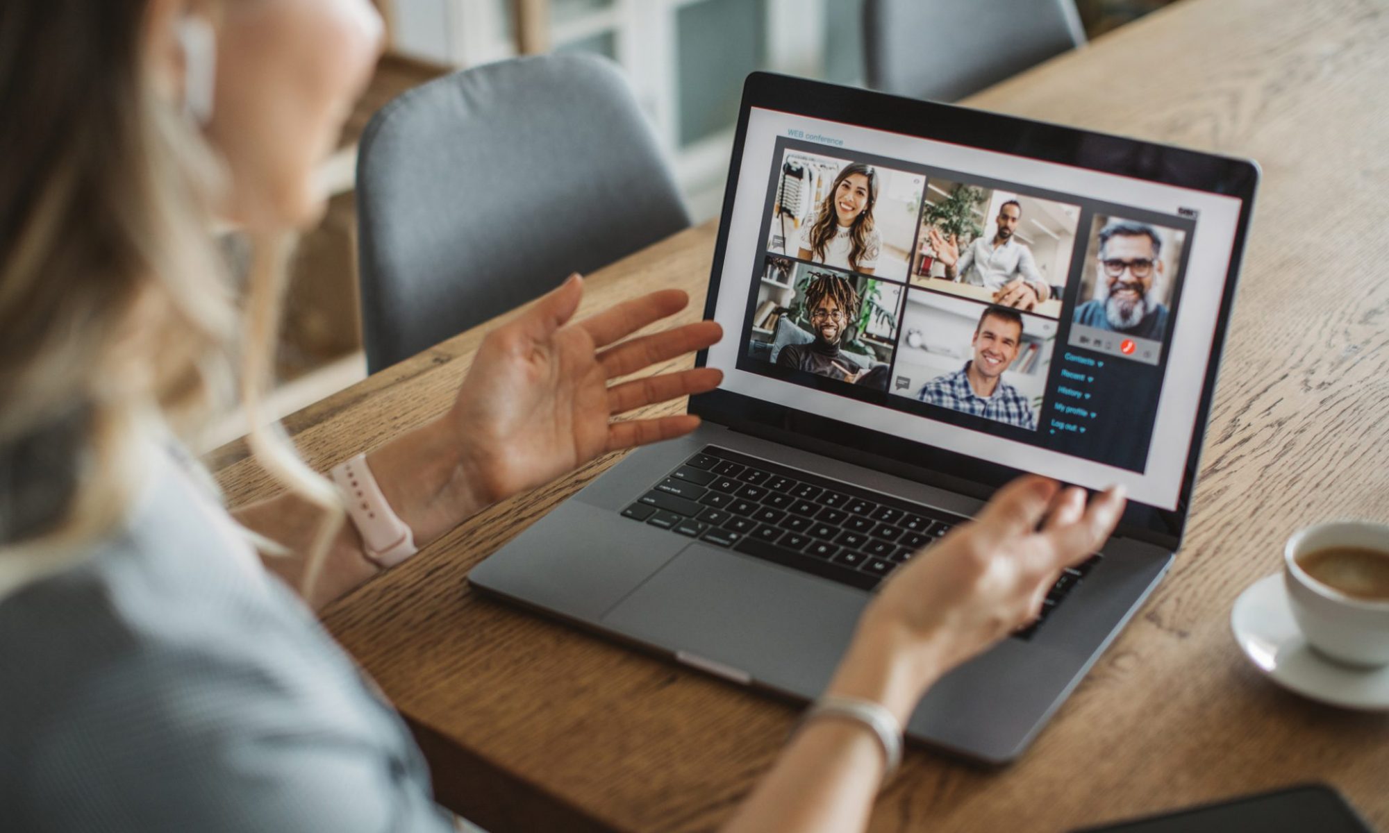 Business Impact article on creating a high-performing hybrid workplace: what should leaders do? A person is having a remote team meeting on the laptop. The individual is working from home engaging with peers. Next to her laptop sits a small shot of espresso.