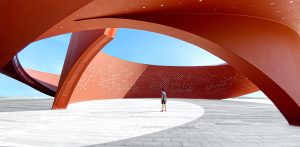 A person standing in a red curved abstract architectural space, 3D rendering. This is symbolic to being more than just digital.