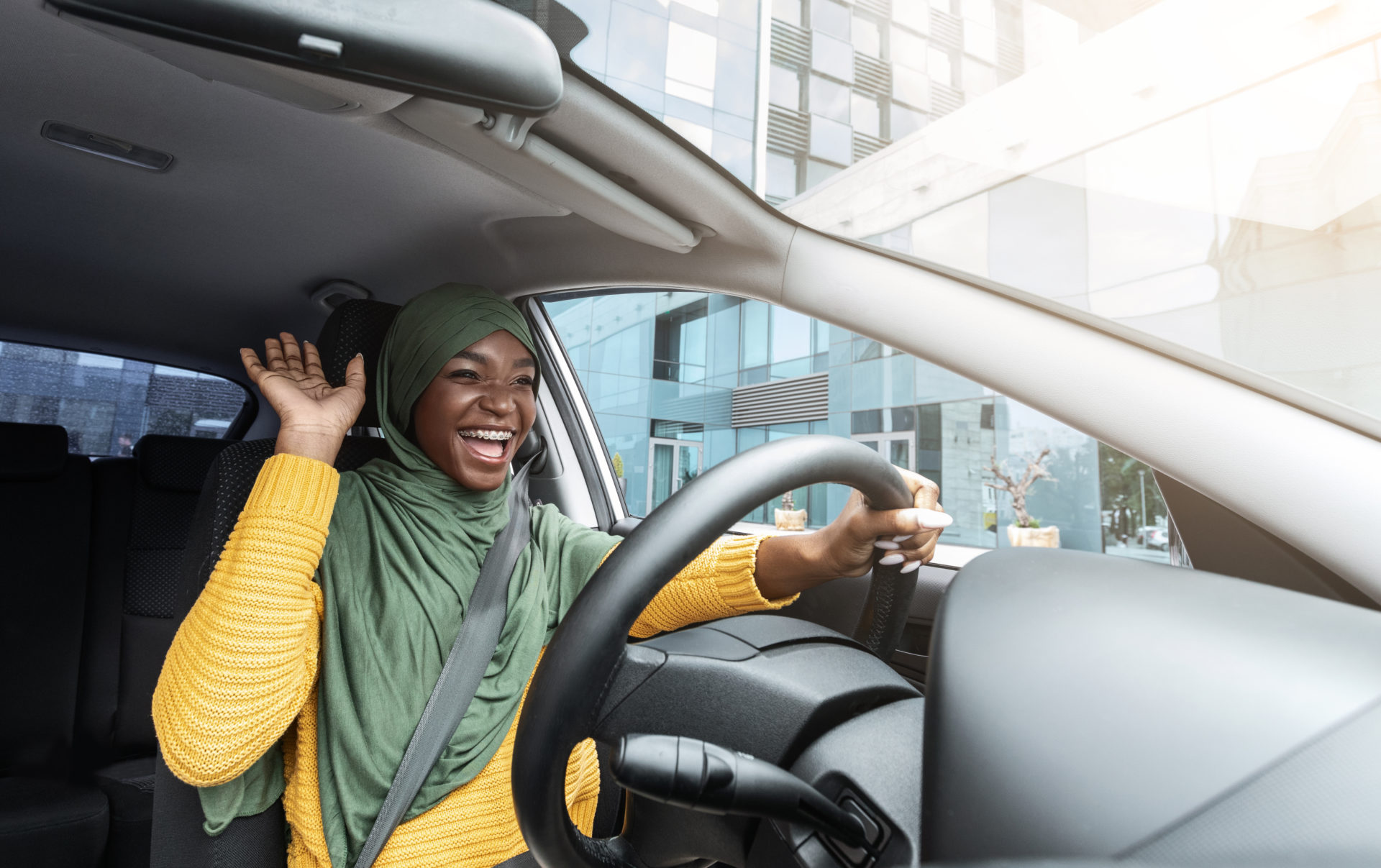 An African female student wearing hijab, happy and driving.