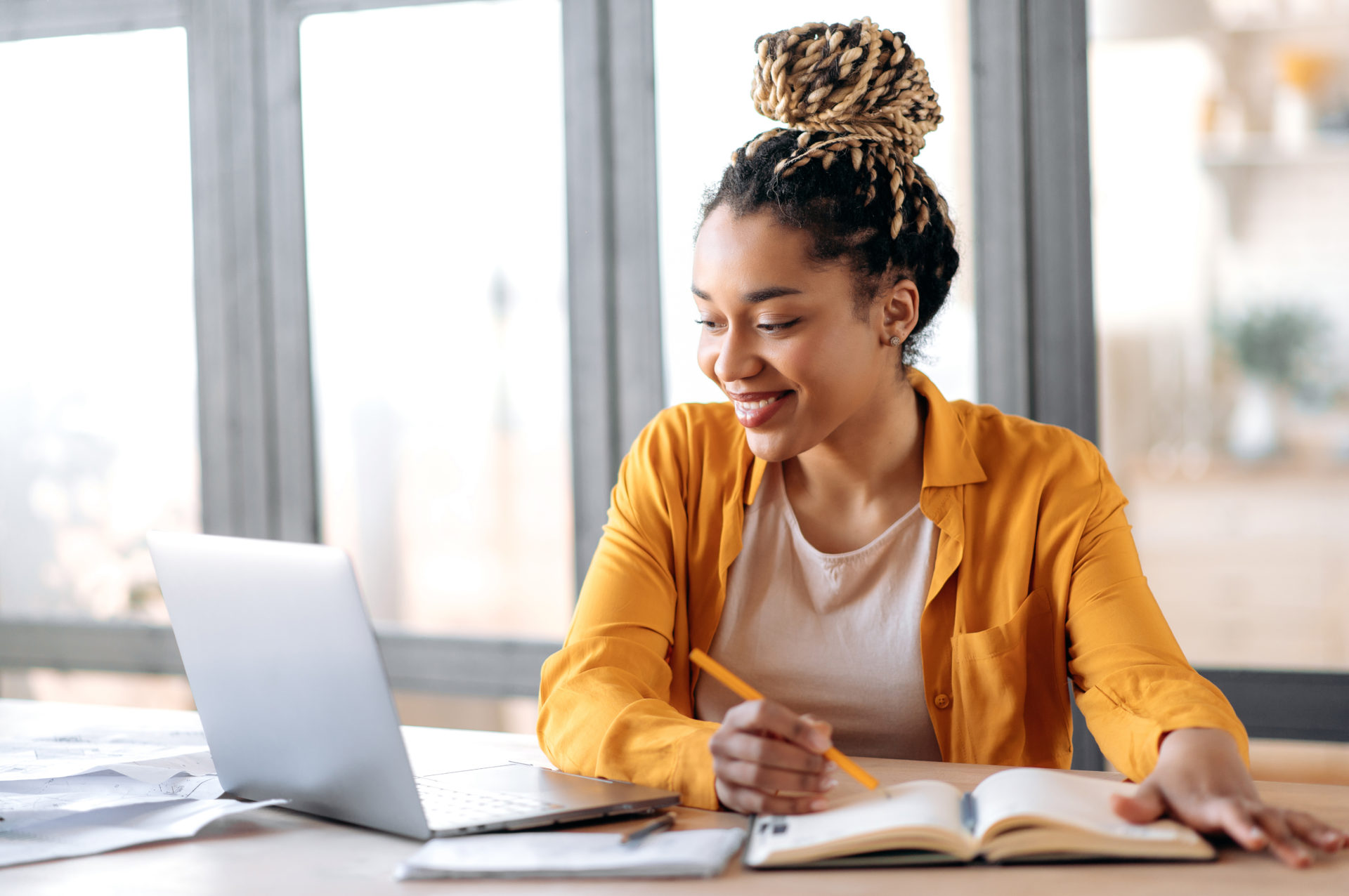 Online webinar, e-learning. Happy african american young woman in stylish casual clothes, studying remotely, using a laptop, listening to online webinar, taking notes while sitting at home, smiles. BGA Career Month 2022.