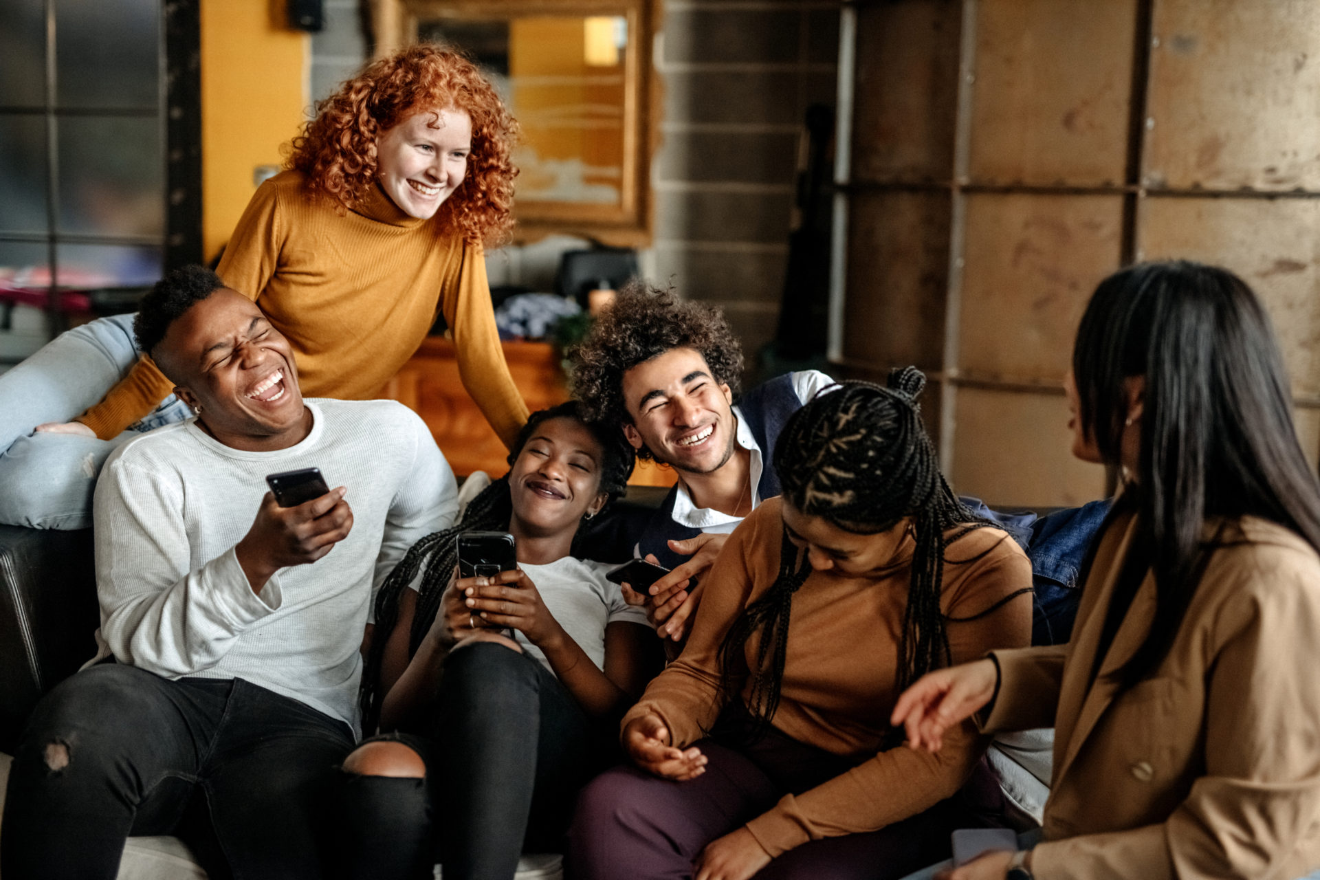 Group of millennial multi-ethnic students sitting on sofa at apartment and laughing. Social event. BGA Careers Month 2022 for students and graduates.