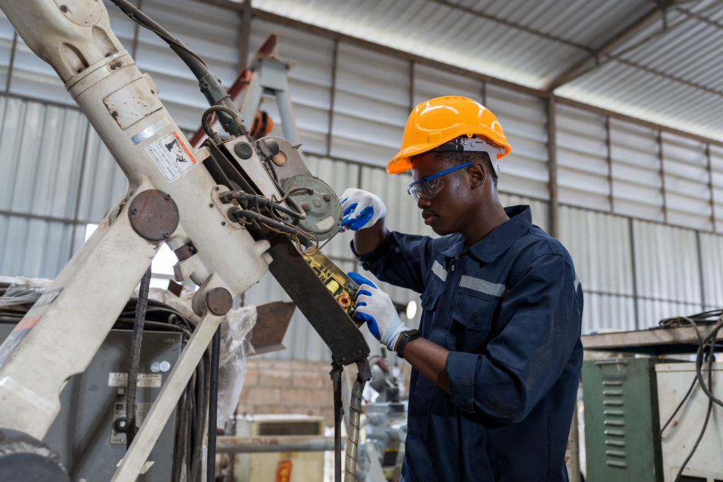 African American factory male engineer worker working with adept robotic arm in workshop. Male engineer maintenance automatic robotic arm machines in factory. Industry robot manufacturing technology